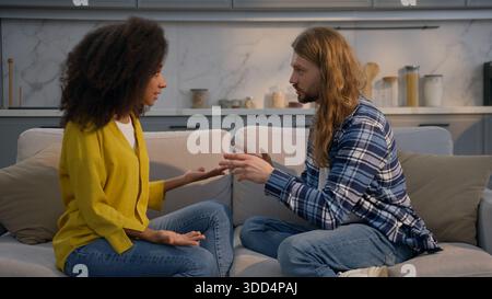Coppia multirazziale in conflitto a casa sul divano uomo caucasico donna africana arrabbiata discutendo di problemi di mutuo assicurativo litigare tradimento Foto Stock