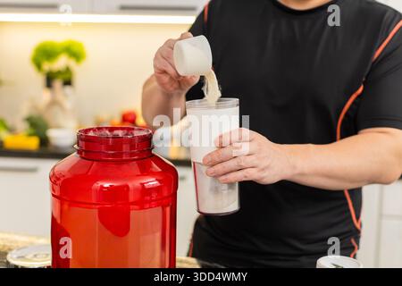 Man aggiunge polvere proteica di siero di latte in piccolo agitatore in cucina prima dell'allenamento. Bevanda integratore sportivo supporta il recupero muscolare equilibrio energetico dieta sana routine per fitness stile di vita palestra. Foto Stock