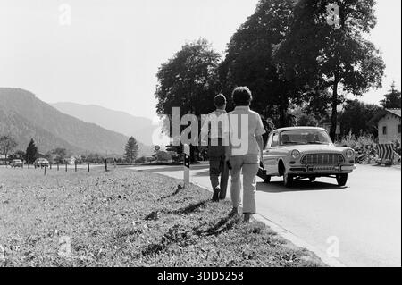 Sessanta, 13.09.1966, Rottach Egern sul lago Tegernsee, paesaggio alpino, catena montuosa, autostrada federale B307, l'automobile viene da Kreuth e guida verso Rottach-Egern, turisti che camminano lungo la strada, coppia, uomo e donna da 30 a 40 anni, Alpi Bavaresi, alta Baviera, Baviera, Germania Foto Stock