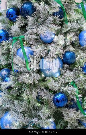 Primo piano di un albero di Natale decorato con ornamenti blu, nastri verdi e luci bianche. Foto Stock