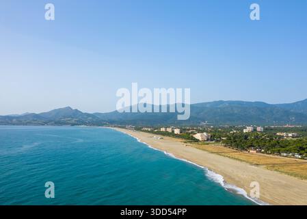 Ampia vista aerea di Argeles con sabbia dorata che incontra le vibranti acque turchesi, sostenute da verdi colline e un cielo azzurro. La costa sembra aperta e invitante, con un'atmosfera estiva rilassata. Foto Stock
