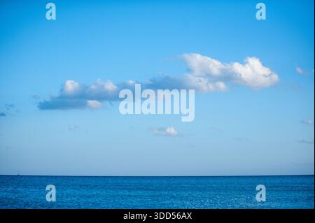 Mare e cielo blu con nuvole bianche sparse su un orizzonte oceanico calmo, paesaggio marino tranquillo estivo Foto Stock