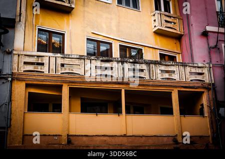 Antica facciata giallo ocra con balconi in legno rustici chiusi e finestre con persiane, architettura di vecchia città mediterranea Foto Stock