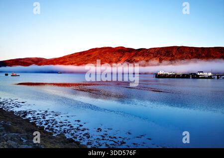 Una splendida alba sul lago Linnhe vicino a Fort William, dove cieli blu profondi e acque calme contrastano perfettamente con il bagliore rosso delle montagne circostanti delle Highland Foto Stock