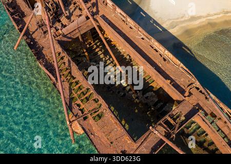 Vista aerea dello scafo arrugginito e scheletrico del relitto di Dimitrios in acque poco profonde e trasparenti vicino a una spiaggia sabbiosa di Gythio, Grecia. La luce del sole rivela complesse texture corrose e la struttura metallica decaduta. Foto Stock