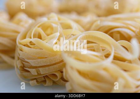 Un macro shot dettagliato di tagliatelle crude, splendidamente disposte in bobine dorate. L'immagine evidenzia la trama e il colore naturale del tradit Foto Stock