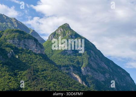 La vetta della montagna, coperta da fitti boschi verdi, si innalza drammaticamente sotto un cielo parzialmente nuvoloso nel massiccio dei Bauges, nelle Alpi francesi. Foto Stock
