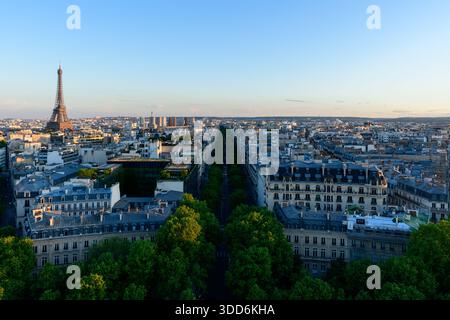 Ampia vista panoramica della Torre Eiffel che si innalza sopra i tetti parigini, con Avenue Kleber fiancheggiata da classici edifici Haussmann e lussureggianti alberi verdi con calda luce serale. Foto Stock