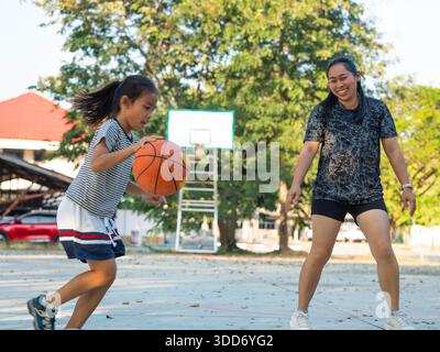 Madre e figlia giocavano a basket insieme su un campo all'aperto durante il tramonto. Foto Stock