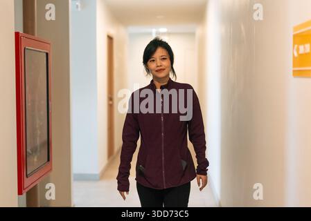 Donna asiatica che cammina nel corridoio, indossa abiti sportivi con un'espressione sicura Foto Stock