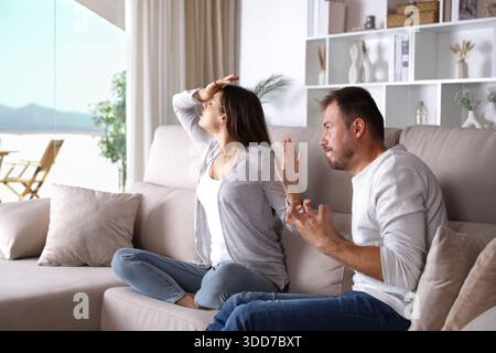 Marito disperato che parla con una moglie drammatica seduta su un divano a casa Foto Stock