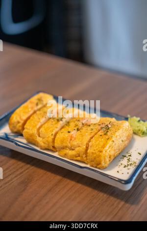 Tamagoyaki, un'omelette giapponese preparata arrotolando diversi strati di uova sbattute fritte, servita su un piatto. Foto Stock