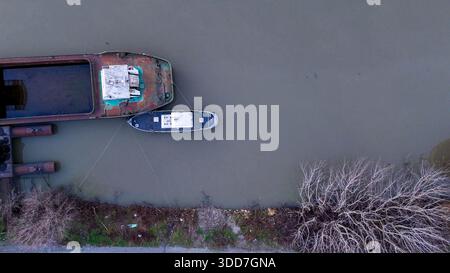 Il po che mostra una vista aerea di una chiatta industriale abbandonata con una gru attaccata, che accumula inquinamento plastico e detriti vicino alla sponda del fiume, Foto Stock