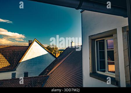 Una vista pittoresca da una finestra che cattura i tetti di un affascinante villaggio sotto un cielo vibrante. Foto Stock