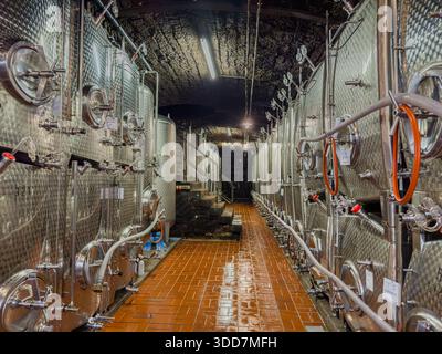 Una vista su un corridoio fiancheggiato da vasche di acciaio inossidabile in una cantina, che mostra la tecnologia moderna utilizzata nella vinificazione. Foto Stock