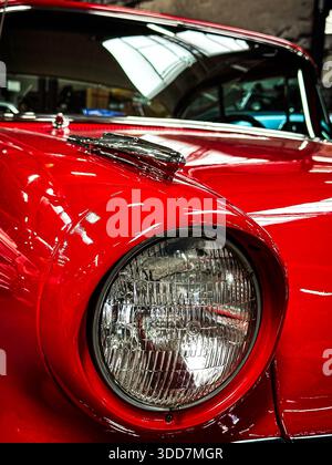 Un primo piano dettagliato del faro di un'auto rossa d'epoca, che mostra il suo design classico e la superficie riflettente. Foto Stock