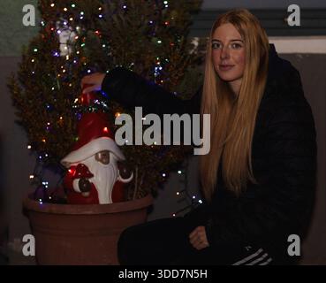 Questa fotografia cattura una giovane donna durante un servizio fotografico di Natale. È posizionata di fronte a un albero di Natale decorato, illuminato da vibranti Foto Stock