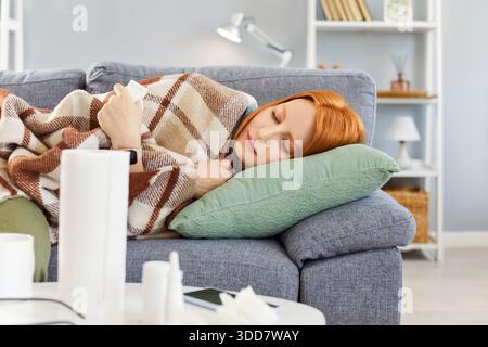 Donna malata sdraiata sul divano avvolta in Una coperta, soffre di malattia a casa Foto Stock