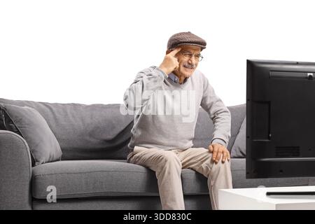 Confuso anziano seduto su un divano a guardare la TV e a tenersi la testa Foto Stock