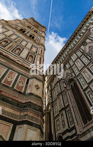 Questa prospettiva verso l'alto cattura il Campanile di Giotto e parte della facciata del Duomo di Firenze sotto un vivace cielo blu, con un percorso di moto d'acqua visibile enha Foto Stock