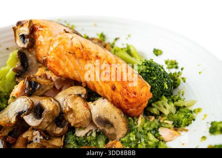 Un filetto di salmone poggia su un letto di broccoli e funghi su un piatto bianco. Il piatto sembra appena fatto, servito a pranzo o a cena, mostrando sano Foto Stock