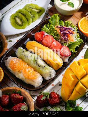 Vivaci involtini primaverili ripieni di frutta assortita, serviti con insalata fresca e decorazioni su un tavolo decorativo. Foto Stock