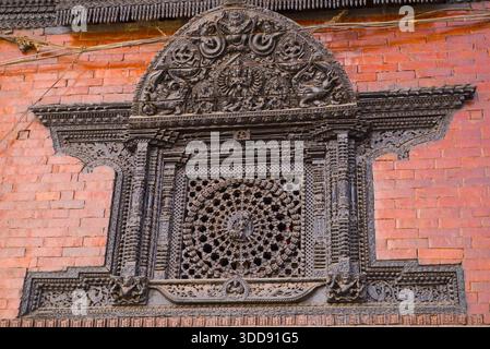 Intricate sculture in legno nepalese su una cornice della finestra in mattoni rossi presso la Kumari House. Foto Stock