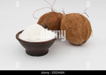 Fiocchi di cocco in recipiente con noci di cocco intere isolate su sfondo bianco Foto Stock
