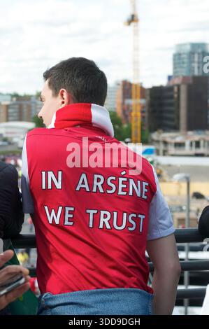 Tifoso di calcio che indossa una giacca dell'Arsenal con lo slogan "in Arsene We Trust", simbolo di lealtà, fede e identità nella cultura calcistica inglese. Foto Stock