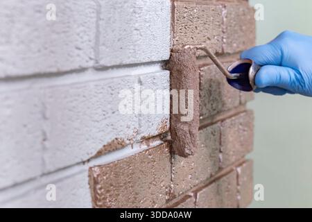 Persona che dipinge su una parete di mattoni grigi con vernice metallica oro rosa utilizzando un rullo per pittura. Fai da te il concetto di miglioramento della casa. Foto Stock