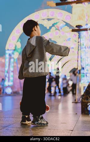 Ragazzo che guarda l'arco illuminato nel festoso mercato notturno - West Lake a Huizhou, provincia del Guangdong, Cina, è un'attrazione turistica caratterizzata da un'architettura antica Foto Stock