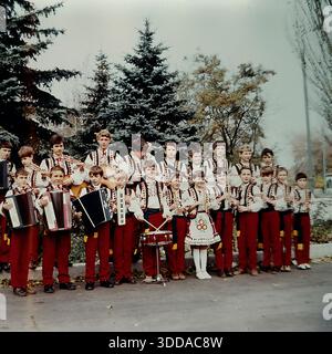 Slaviansk, regione di Donetsk, RSS Ucraina, Unione Sovietica, 1980 Una fotografia a colori d'archivio di un grande gruppo di musica folk per bambini del Palazzo della Cultura dei lavoratori ferroviari (DK ZhD). Posato all'aperto in un parco, il gruppo di studenti indossa costumi tradizionali ucraini. Possiedono vari strumenti musicali: fisarmoniche, chitarre, un tamburo rullante e sopilka in legno. Una ragazza con un abito ricamato sta al centro. Una vivace scena di educazione musicale e patrimonio culturale nel tranquillo Donbas. Foto Stock