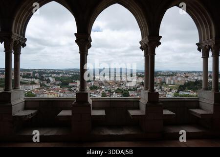 Vista da una struttura architettonica con archi che si affacciano su un paesaggio urbano, con edifici e colline sullo sfondo sotto un cielo nuvoloso Foto Stock