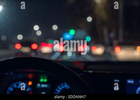 Una prospettiva sfocata dall'interno di un'auto durante il traffico notturno, che mostra luci rosse e bianche di veicoli e lampioni sullo sfondo. Foto Stock