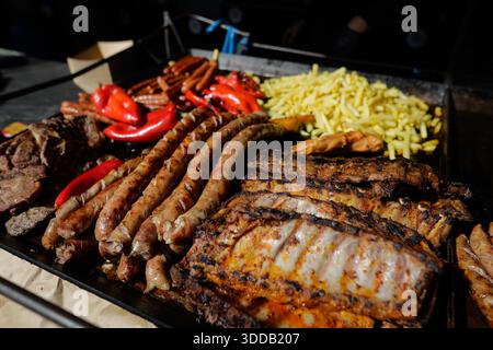 Prodotti a base di carne (mici, costolette di maiale, salsicce, patatine fritte) su una griglia esterna in metallo carbone. Foto Stock
