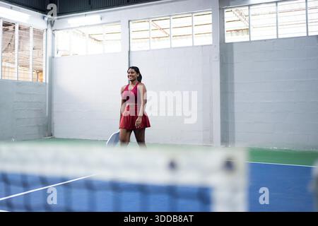 Giocatrice di paddle sorridente che cammina su un campo al coperto con la sua racchetta Foto Stock