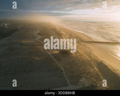 Vista aerea delle sabbie dorate che incontrano il mare turbolento sotto un cielo nebuloso, sentieri sulla spiaggia che si snodano tra le dune, Seignosse le Penon, Francia. Foto Stock