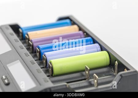 Primo piano di un caricabatterie nero con batterie multicolore. Le batterie sono blu, marrone chiaro, viola e verde e disposte in fila. Lo sfondo è bianco Foto Stock