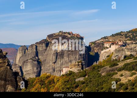 Vista spettacolare dei monasteri di Grand Meteore e Varlaam arroccati su immense colonne di arenaria a Meteora, in Grecia, circondati da fogliame autunnale sotto un cielo azzurro. Foto Stock