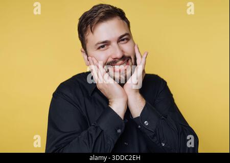 Uomo sorridente in camicia nera che posa su uno sfondo giallo. Foto Stock