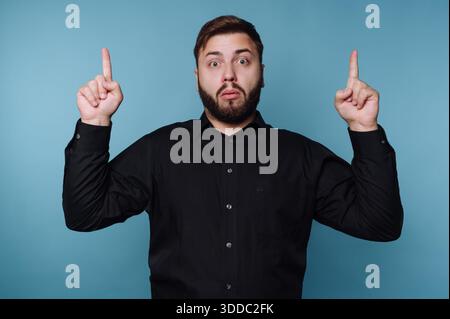 Uomo in camicia nera rivolta verso l'alto con un'espressione sorpreso Foto Stock