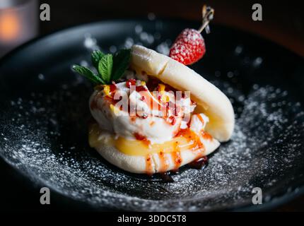 Un dessert con una fragola in cima e una foglia verde a lato. Il dessert è servito su un piatto nero Foto Stock