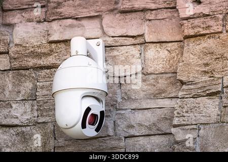 Telecamera di sicurezza montata su un muro di pietra ruvida, che fornisce sorveglianza e mette in risalto la tecnologia di sicurezza e monitoraggio Foto Stock