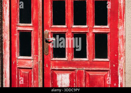 Porta in legno resistente agli agenti atmosferici che mostra una vivace vernice rossa e piccoli pannelli delle finestre, con una maniglia in ottone vintage Foto Stock