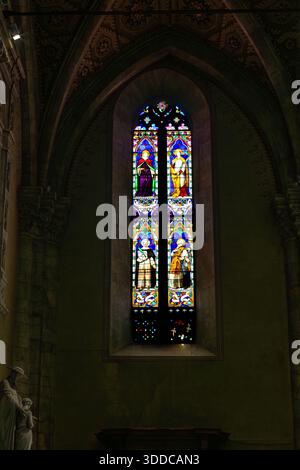 Un'alta e vibrante vetrata all'interno di una chiesa gotica, che proietta luce colorata sulle pareti in pietra. La scena trasmette riverenza, fede e tempo Foto Stock