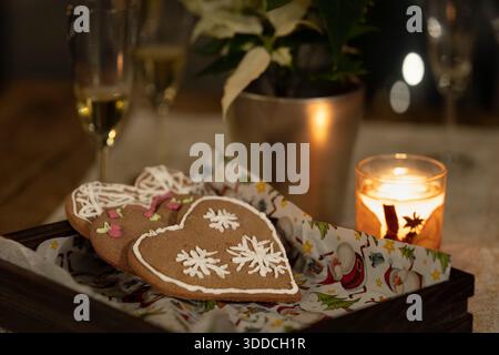 Biscotti di pan di zenzero a forma di cuore con glassa bianca serviti a lume di candela in un ambiente accogliente e festoso. Una vacanza calda natura morta con pane di zenzero decorato. Foto Stock
