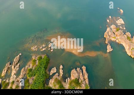 La prospettiva aerea rivela affioramenti lisci di arenaria, rocce sparse e fondali sabbiosi nel tranquillo fiume Mekong vicino a Champassak, nel Laos meridionale. La calda luce del giorno mette in risalto le texture naturali, il verde sottile e le acque cristalline blu-verdi in questo vasto paesaggio fluviale. Foto Stock