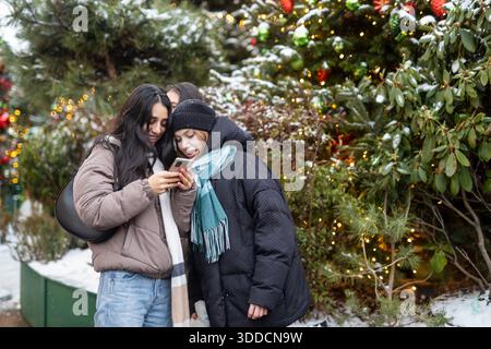 Mosca, Russia, 29 dicembre 2025 amici che usano lo smartphone all'aperto in inverno. Foto Stock
