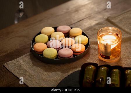 Colorato assortimento di macaron francesi disposti su un piatto su un tavolo di legno. Macaron pastello con ripieno cremoso serviti con luce naturale. Foto Stock