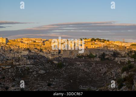 La luce soffusa e dorata inonda gli edifici in pietra di Matera, mettendo in risalto la città storica arroccata su aspri terreni rocciosi sotto un cielo con nuvole stratificate. Foto Stock